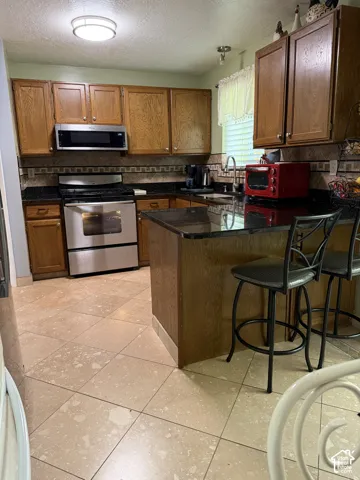 Kitchen featuring stained wood cabinetry, stone-finish countertops, stainless steel appliances, and a breakfast bar