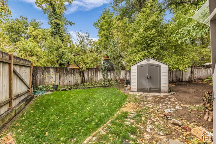 Private backyard featuring a fenced perimeter, expansive lawn, stone-paved walkway, and detached storage structure