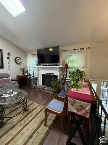 Vaulted ceiling with skylight, fireplace with a mantel, and wood-finish flooring