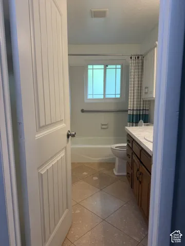Bathroom featuring tile flooring, wood-finish cabinetry, a solid-surface countertop with an integrated sink, a tiled shower surround with a grab bar, and a window
