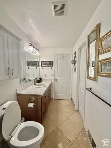Bathroom featuring a wood vanity with a stone-finish countertop, integrated round sink, polished metal faucet, wall-mounted light fixture, and tile flooring