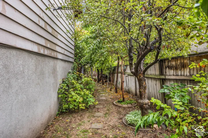 Side yard featuring horizontal lap siding, stucco foundation, wood fencing, and mature trees with stone paver path