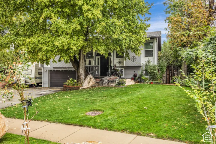 Split-level exterior featuring a combination of horizontal and vertical siding, attached garage, stone landscaping accents, and mature foliage