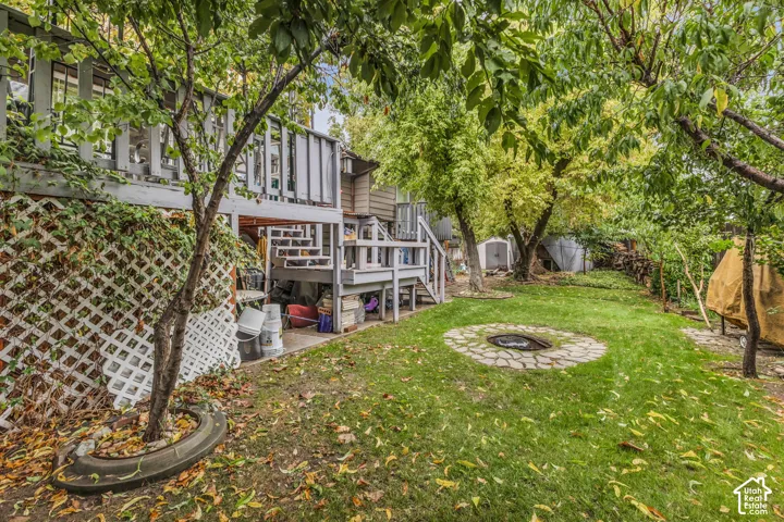 Backyard featuring a raised wooden deck, lattice privacy skirting, stone-ringed fire pit, and mature trees