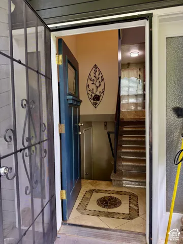 Entryway featuring a decorative wrought-iron storm door, a solid-panel door with a glass inset, custom stone-tile flooring with a circular medallion inlay, and a staircase with metal railings