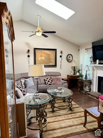 Vaulted ceiling featuring a central skylight, wood-finish flooring, and a fireplace with a mantel