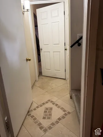 Ceramic tile flooring with decorative stone inlay, six-panel interior doors, wall-mounted light fixture, and metal handrail