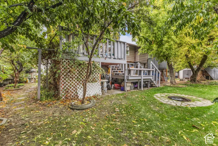 Multi-level wooden deck with attached staircase, lattice privacy screen, and stone-accented fire pit area situated within a tree-lined lot