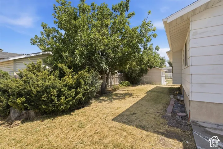 Side yard area featuring horizontal siding, mature shade trees, and a wooden privacy fence