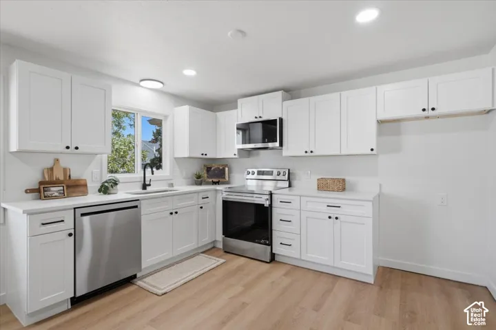 Kitchen featuring white shaker-style cabinetry, stainless steel appliances, solid-surface countertops, recessed lighting, and wood-finish flooring