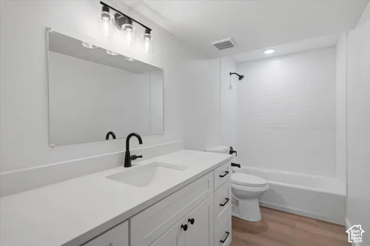 White vanity featuring a solid-surface countertop with an integrated basin, matte black hardware, a tiled tub-shower combination, and wood-finish flooring