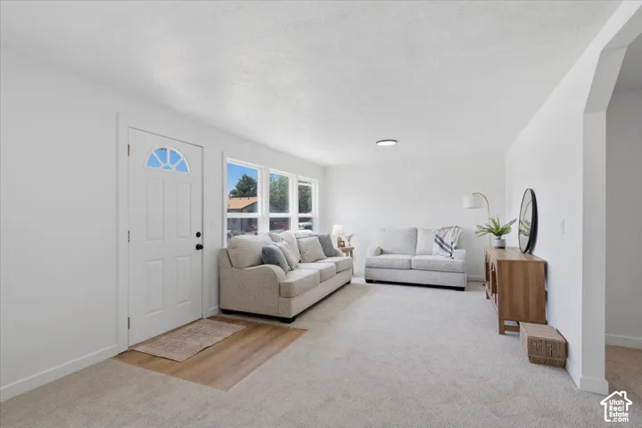 Neutral interior featuring broad windows, a multi-panel exterior entry door with a decorative window insert, wood-finish flooring at the threshold, and carpeted flooring