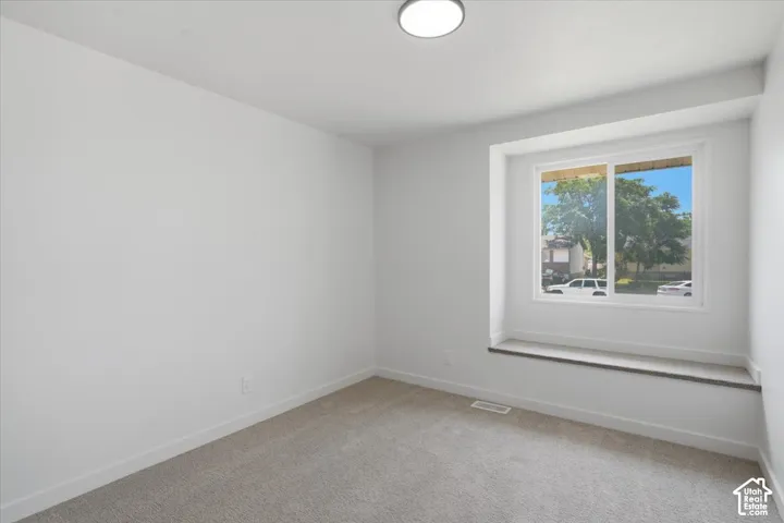 Interior space featuring neutral-toned carpeting, a recessed window nook with a built-in ledge, a sliding glass window, and flush-mount ceiling lighting