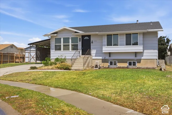 Exterior featuring light-colored horizontal siding, asphalt shingle roofing, a front-facing bay window, concrete steps with metal handrails, and a covered carport
