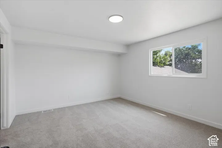 Neutral-toned wall-to-wall carpeting, crisp white walls, flush-mount LED ceiling lighting, and a horizontal sliding window