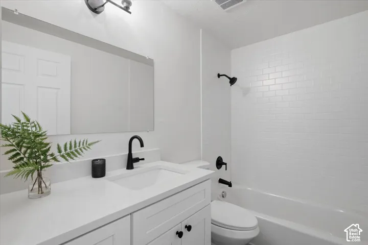 Bathroom featuring a white vanity with a solid-surface countertop, matte black faucet, wall-spanning mirror, and a tub with a white subway-tile surround and matte black fixtures