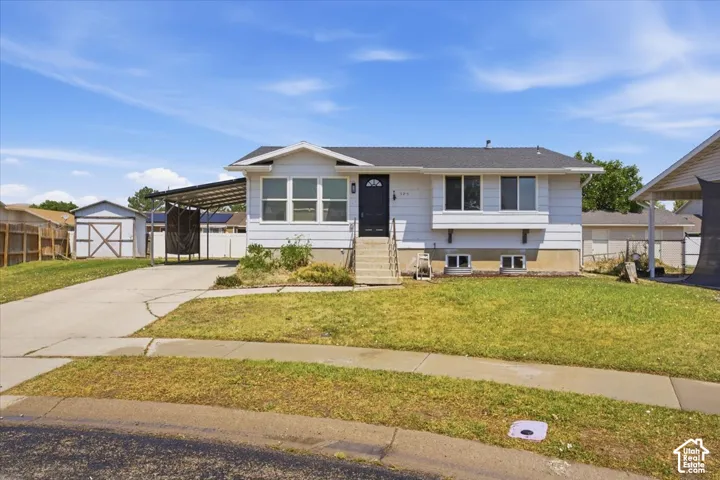 Split-level exterior featuring horizontal siding, a covered carport, a detached storage structure, a concrete driveway, and a front lawn
