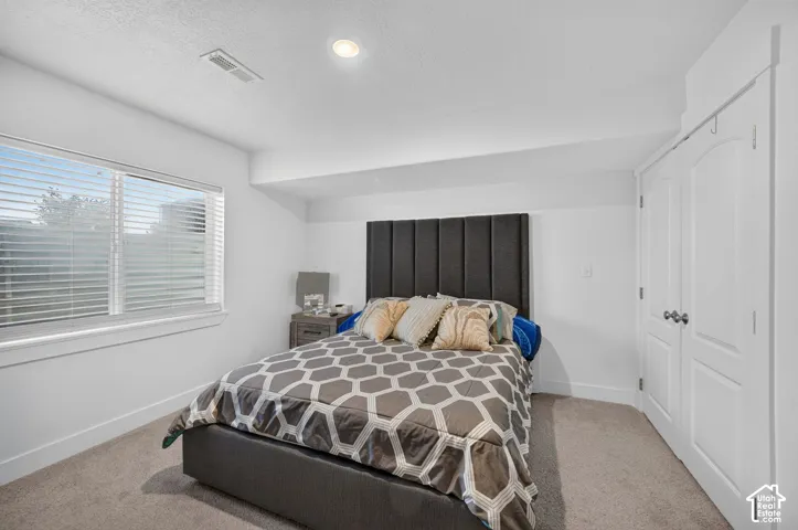 Recessed lighting illuminates this room featuring white walls, a large window with blinds, and durable carpet flooring