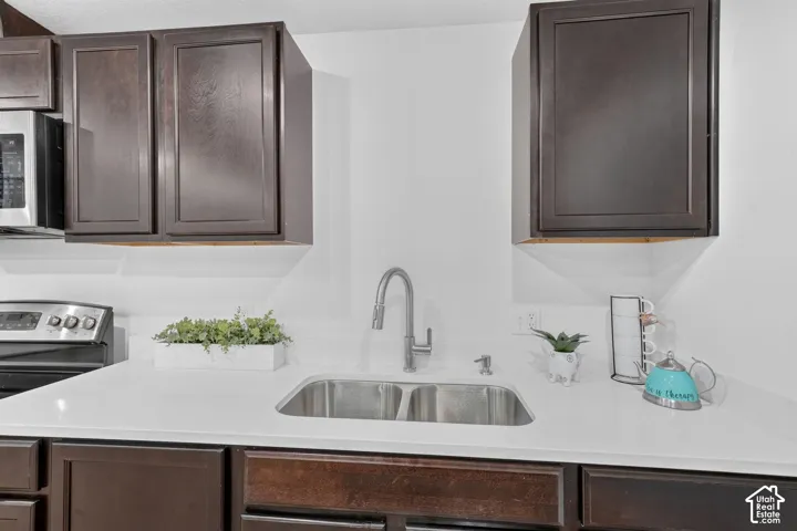 Stainless steel double basin sink with a high-arc faucet, solid surface countertops, and dark wood-finish cabinetry