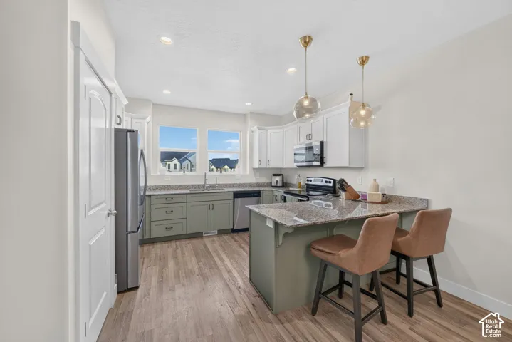 Kitchen featuring wood-finish flooring, two-tone cabinetry, stainless steel appliances, recessed lighting, and an eat-at island with pendant lighting