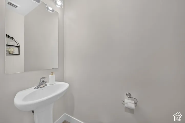 Pedestal sink with chrome faucet, wall-mounted mirror, and overhead vanity lighting