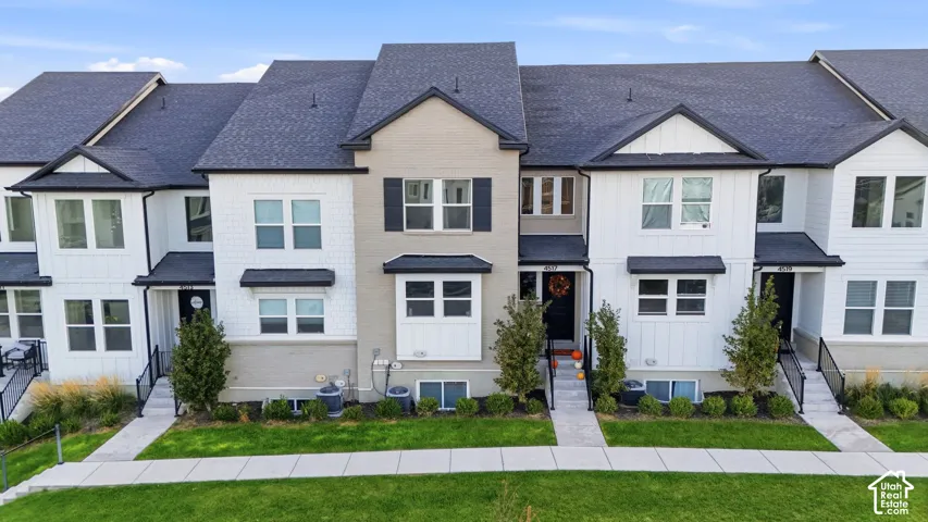 Contemporary townhome exterior featuring a contrasting facade of white siding and light gray brick, multiple large windows, a dark shingle roof, and a neatly maintained front walkway
