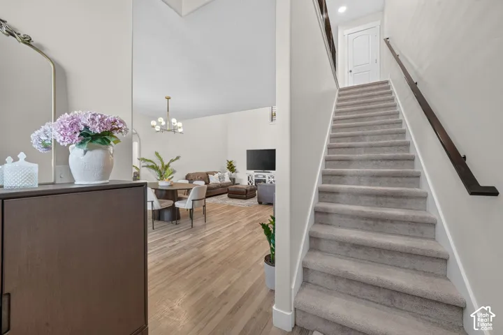 Carpeted staircase with dark wood-finish handrail, wood-finish flooring, and a modern chandelier