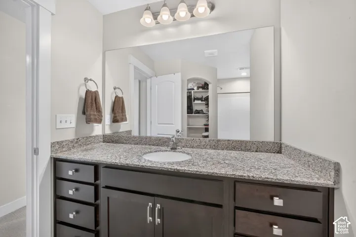 Vanity with a granite countertop, undermount sink, dark wood-finish cabinetry, and brushed nickel hardware