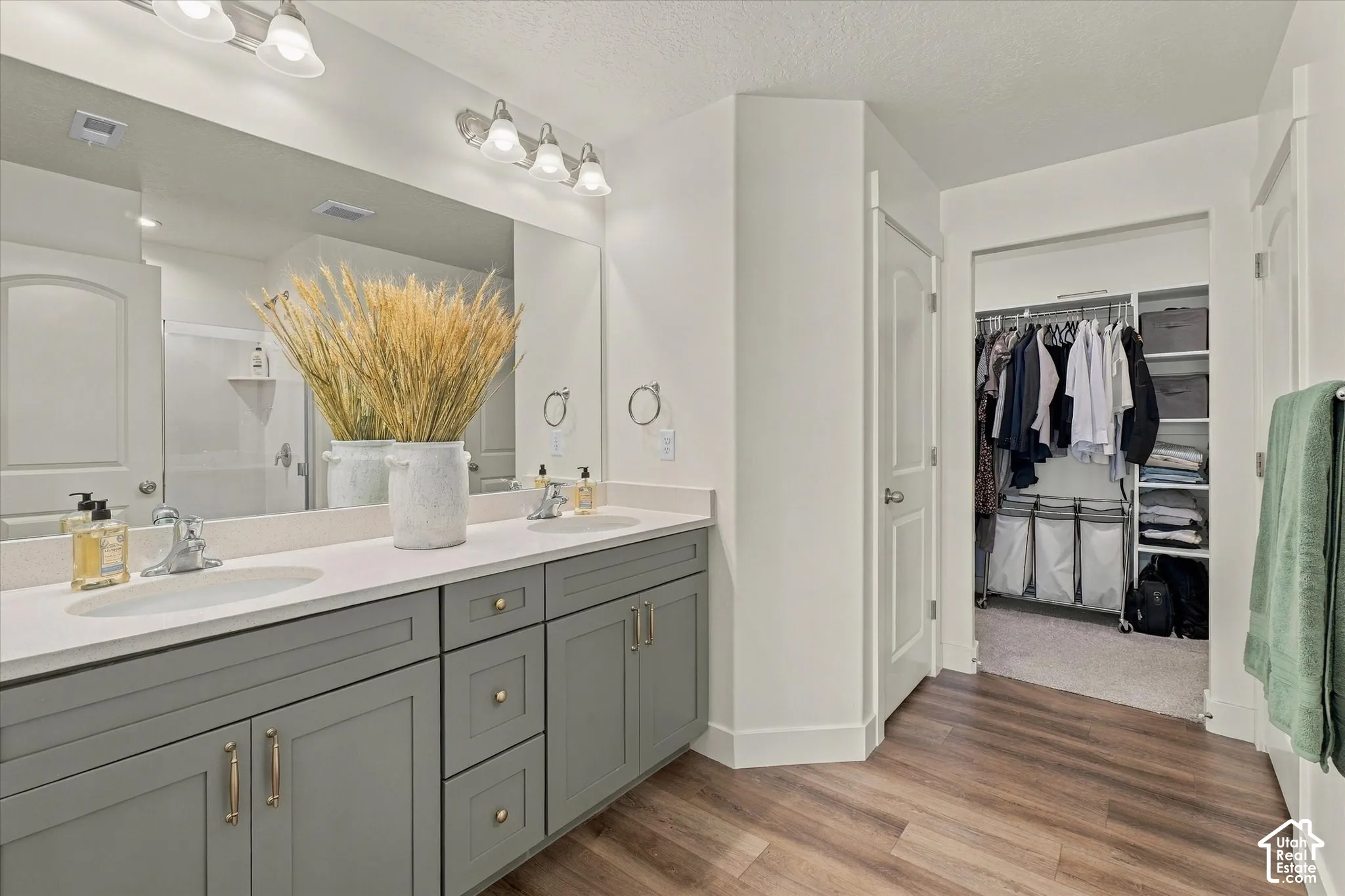 Dual-sink vanity with neutral-toned cabinetry, light-colored countertops, large wall-mounted mirror, and wood-finish flooring