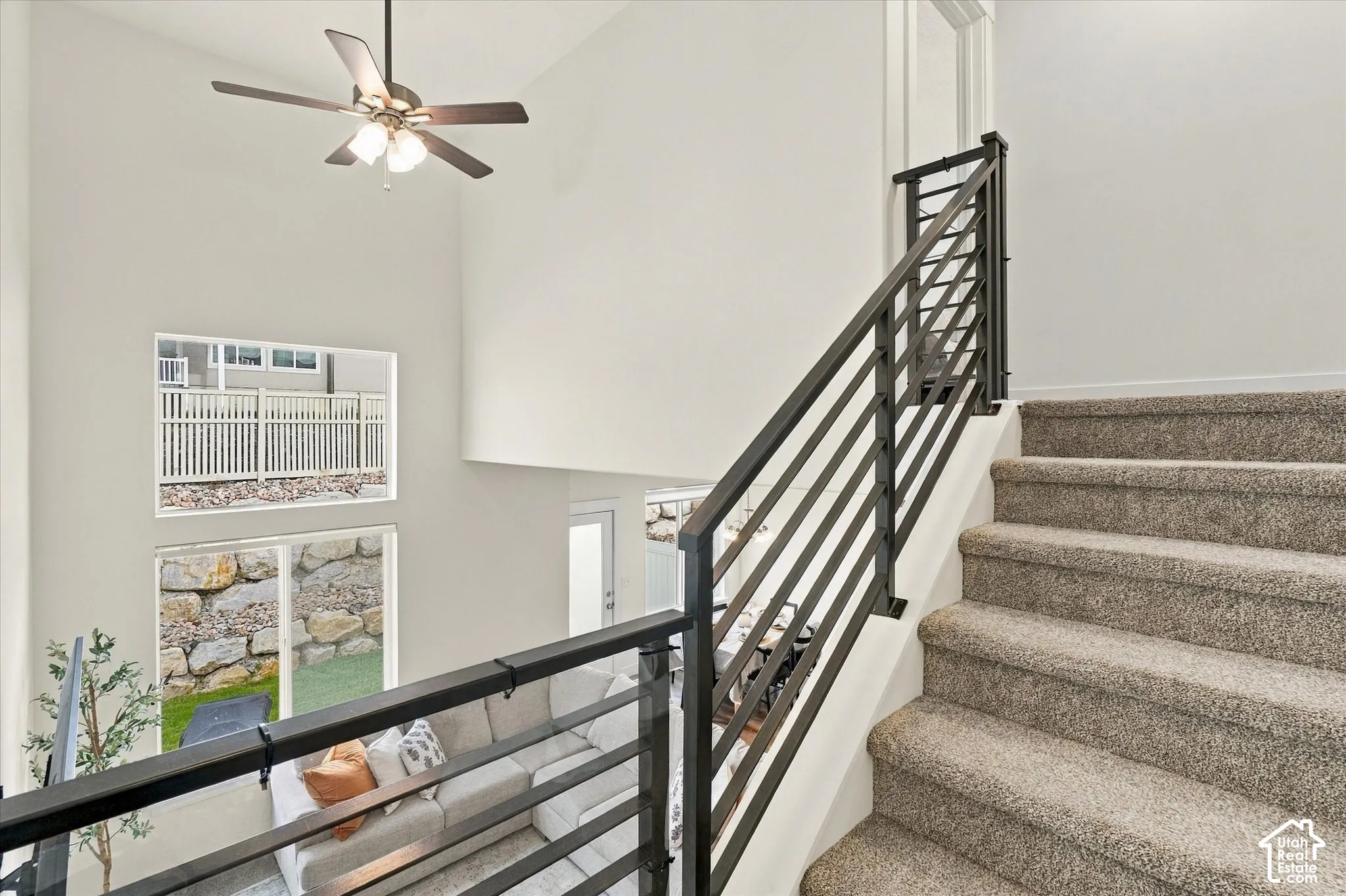 Staircase featuring carpeted steps and a custom metal horizontal-rail banister, soaring vaulted ceilings, a multi-blade ceiling fan, and stacked windows