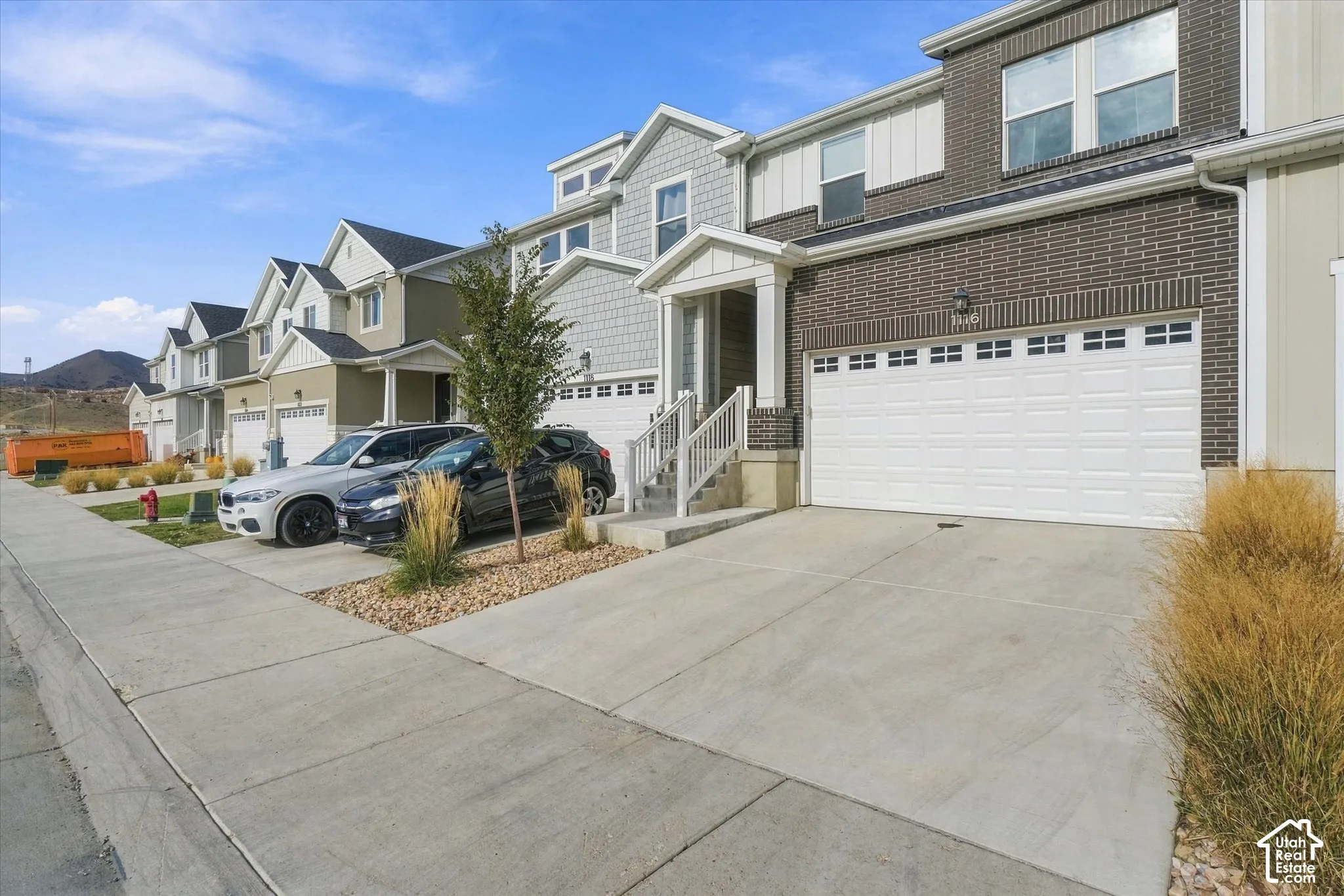 Multi-story townhome exterior featuring brick and siding facade, covered entryway with stairs, concrete driveway, and attached two-car garage