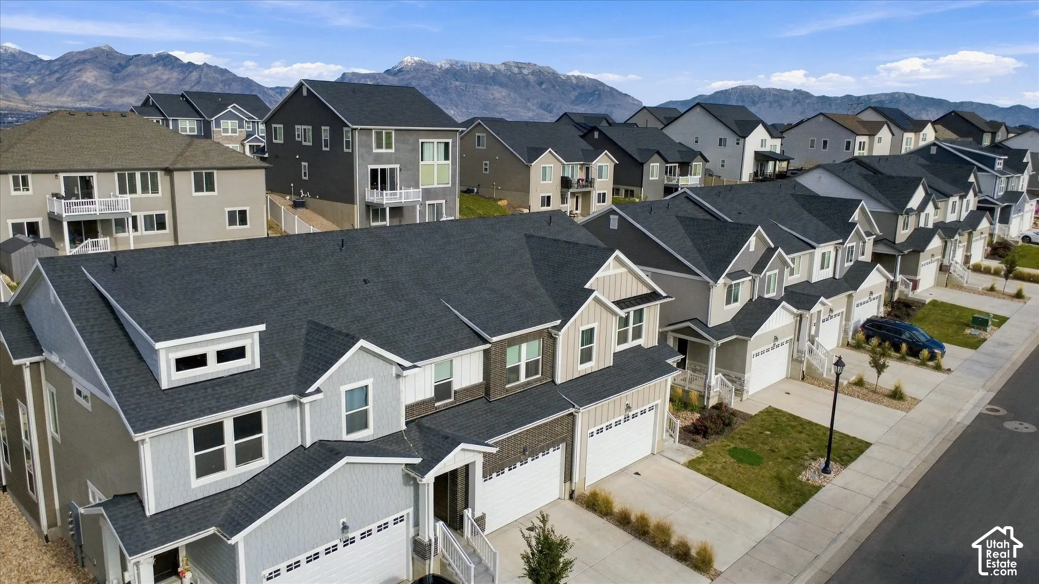 Aerial perspective of a multi-story residence featuring composite shingle roofing, vertical board-and-batten siding, stone veneer accents, multi-car garage, and a mountainous backdrop