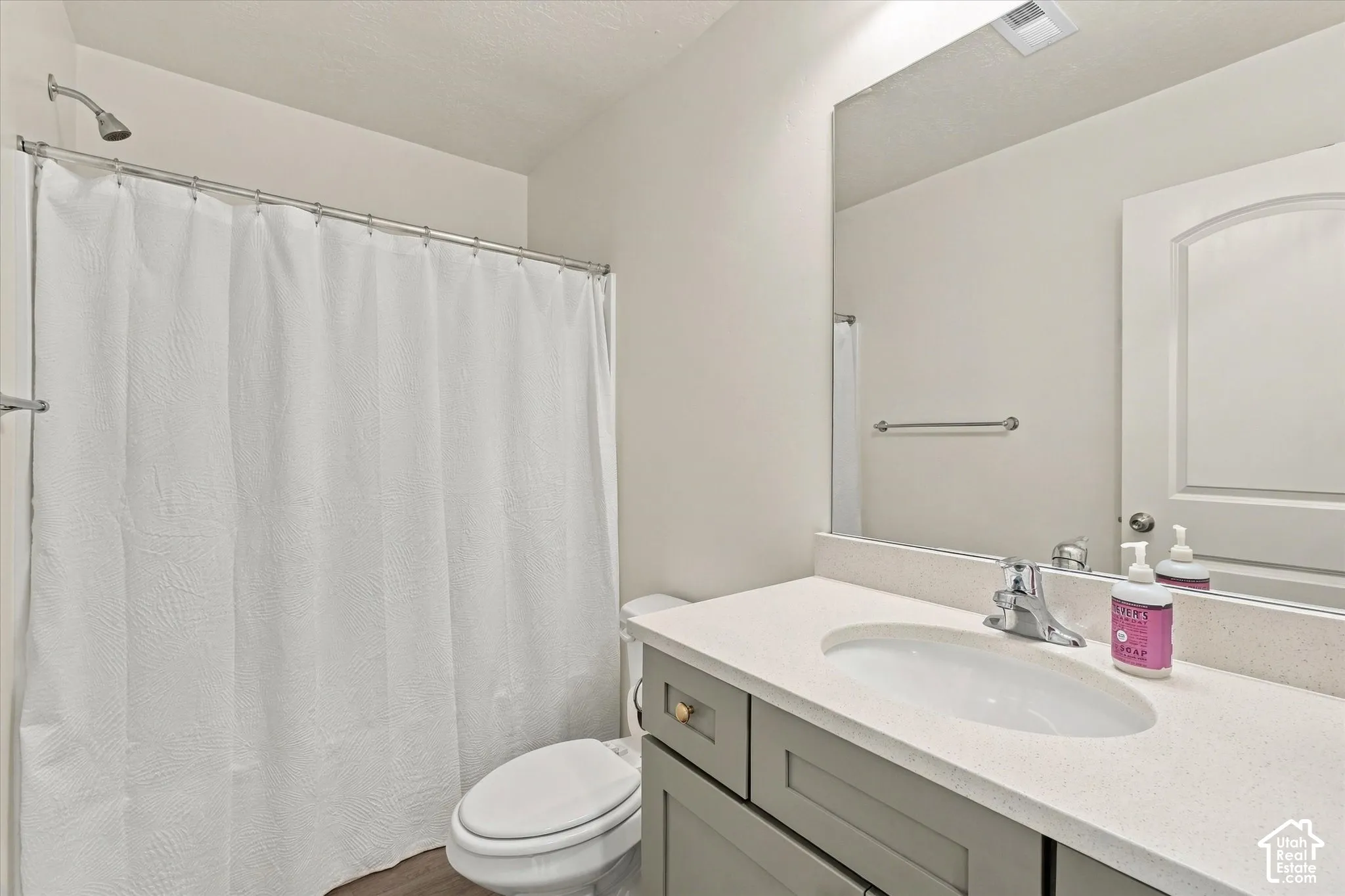 Bathroom featuring a grey vanity with a solid surface countertop, an oval undermount sink, a large wall-mounted mirror, and a shower-tub combination with a chrome fixture