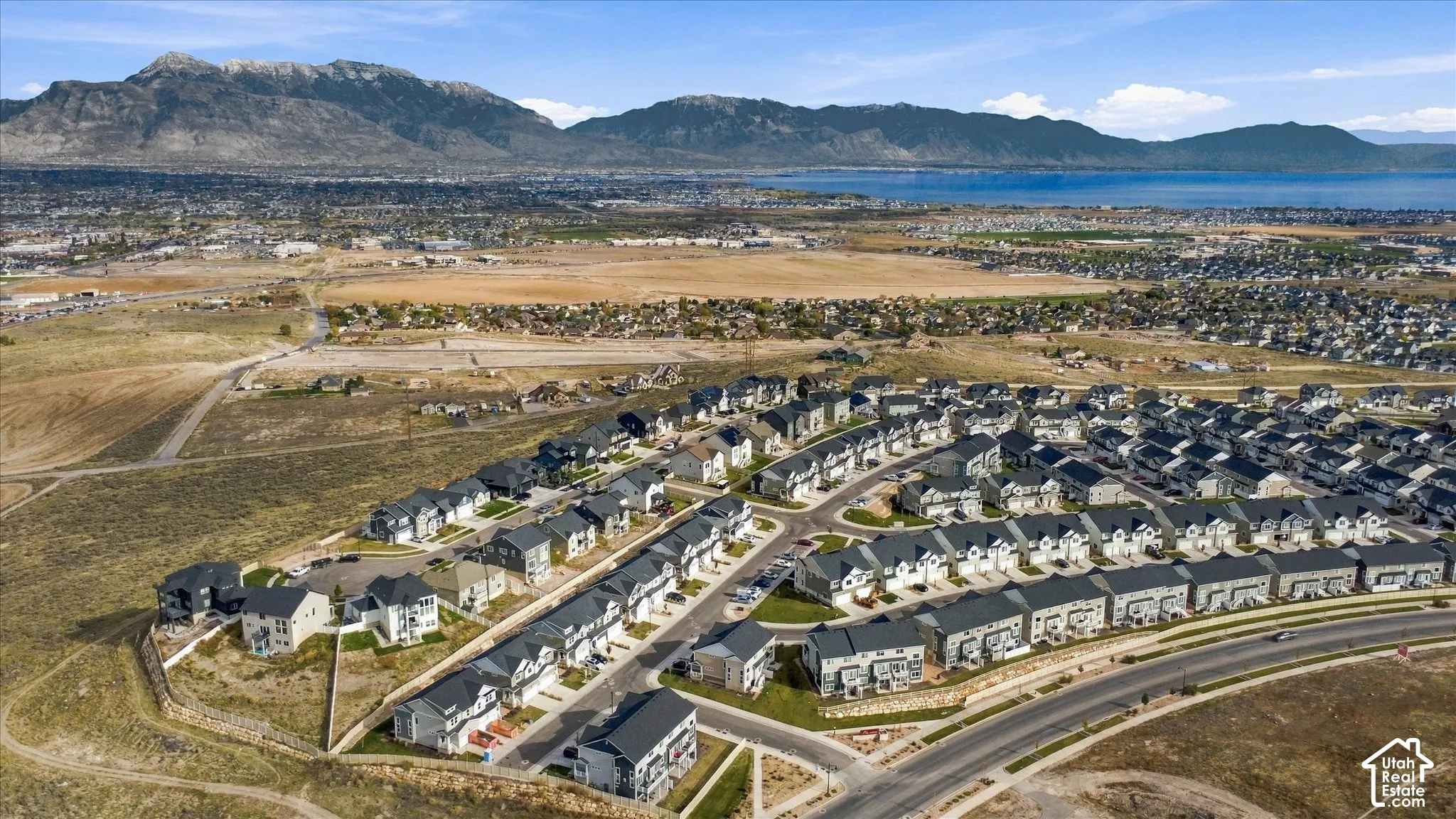 Aerial perspective of a multi-unit residential community featuring pitched rooflines, paved streets, and a mountainous backdrop