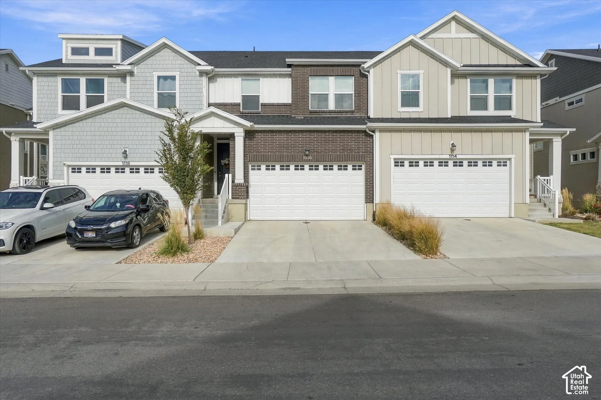 Multi-unit residential exterior featuring a mixed-material facade of brick veneer, horizontal lap siding, and shake shingle accents, complemented by dual-car garages with white sectional doors and covered concrete entryways