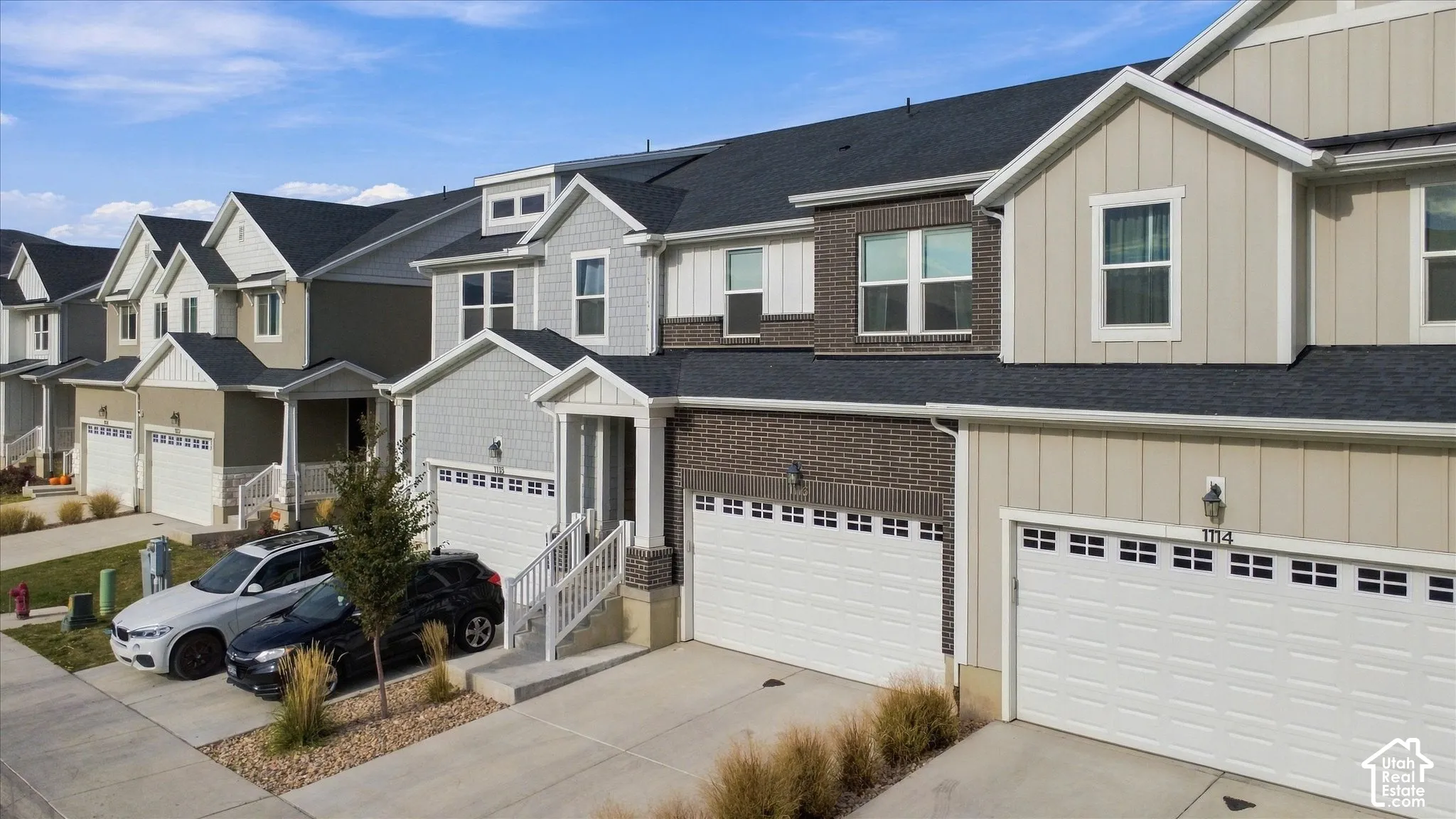 Multi-story townhome exterior featuring brick and vertical siding, pitched rooflines, dual-car garages, and white wooden porch railings