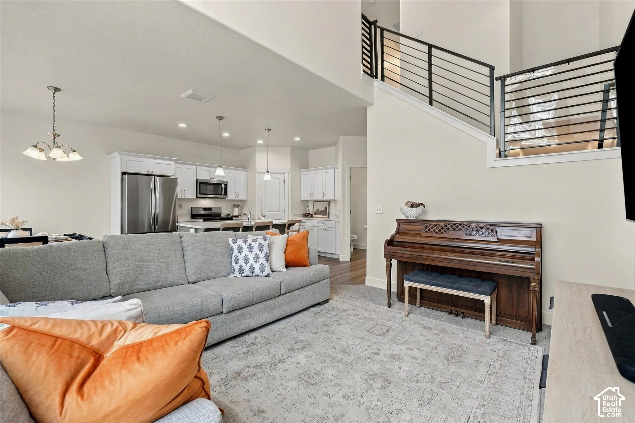 Open-concept floor plan featuring high ceilings, white cabinetry, stainless steel appliances, kitchen island, and metal horizontal-bar staircase railing