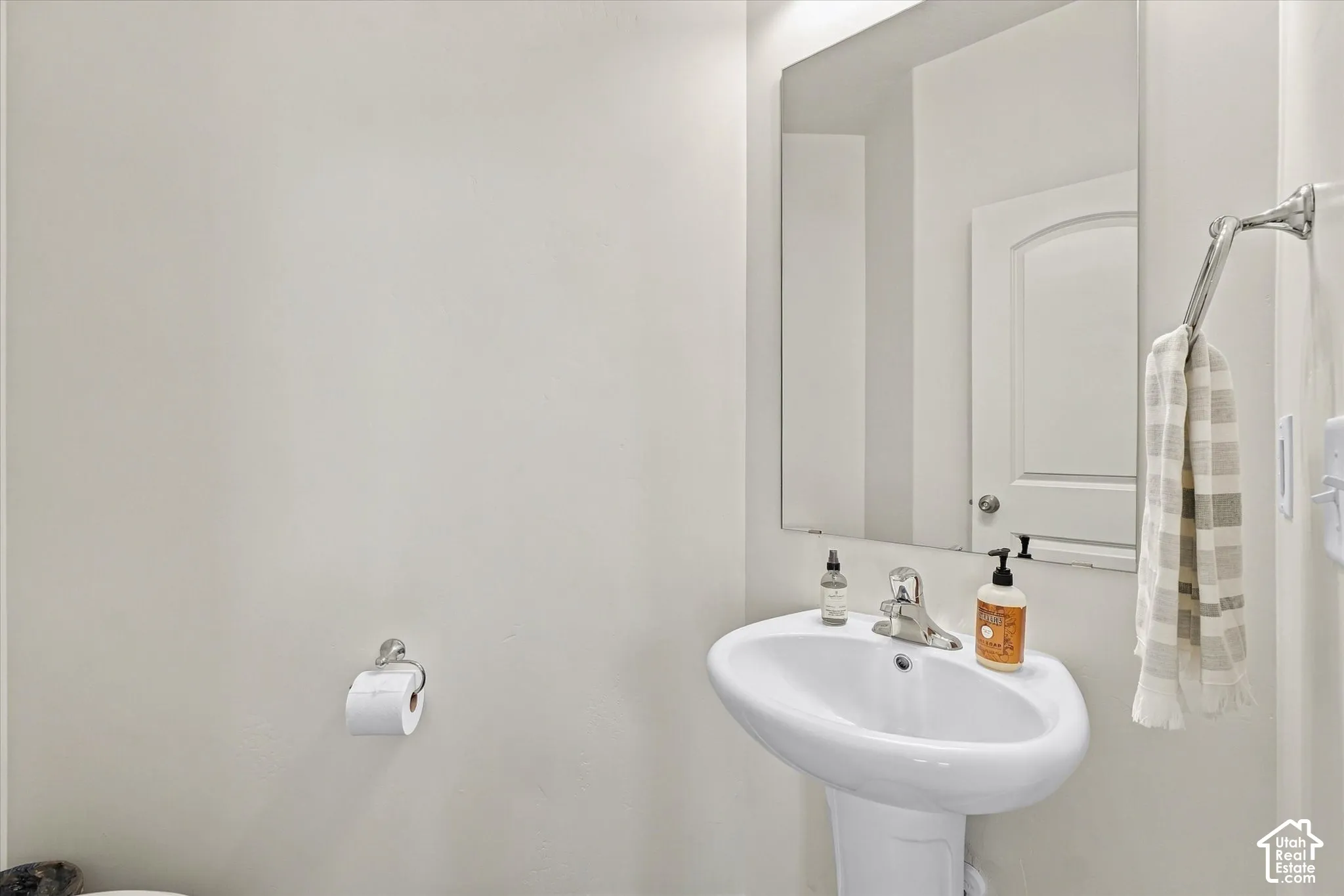 White pedestal sink with a chrome single-handle faucet, large frameless wall mirror, and chrome towel hardware