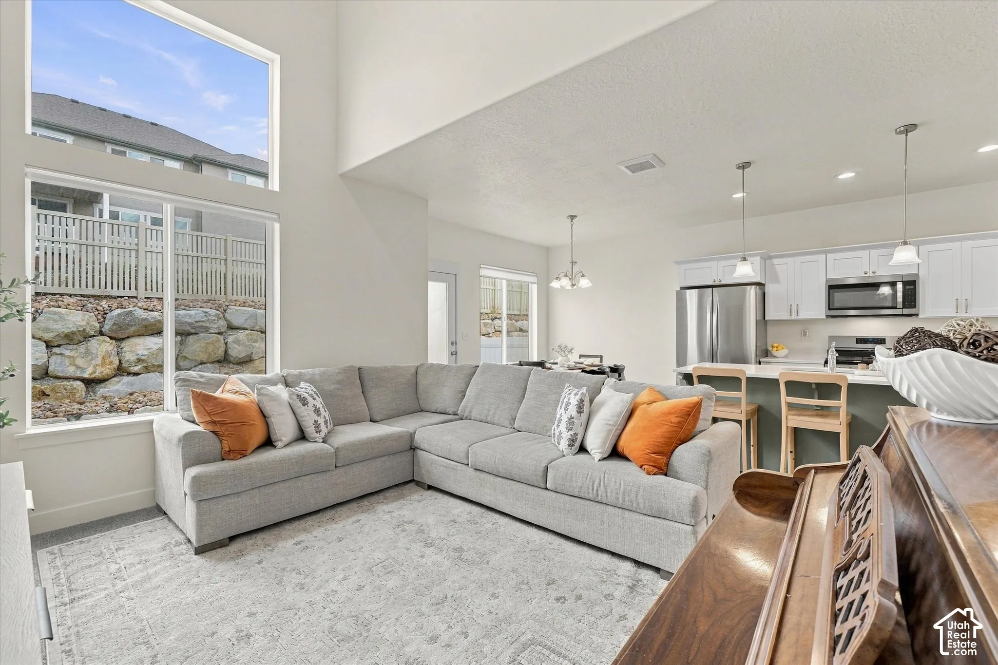 Vaulted ceilings, expansive floor-to-ceiling windows, white cabinetry, stainless steel appliances, and a kitchen island with pendant lighting