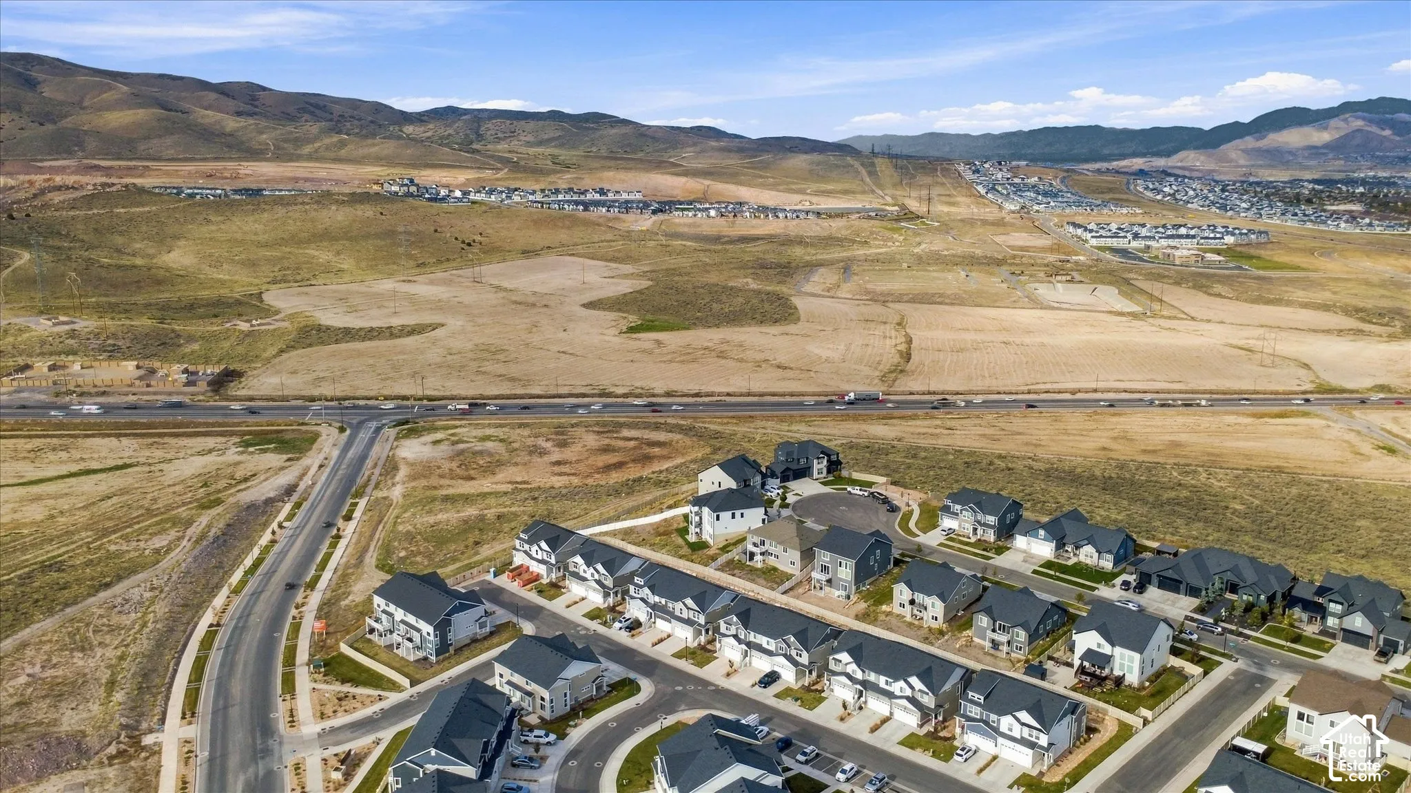 Aerial perspective of residential community featuring multi-level dwellings with pitched roofs, paved streets, and expansive mountain terrain backdrop