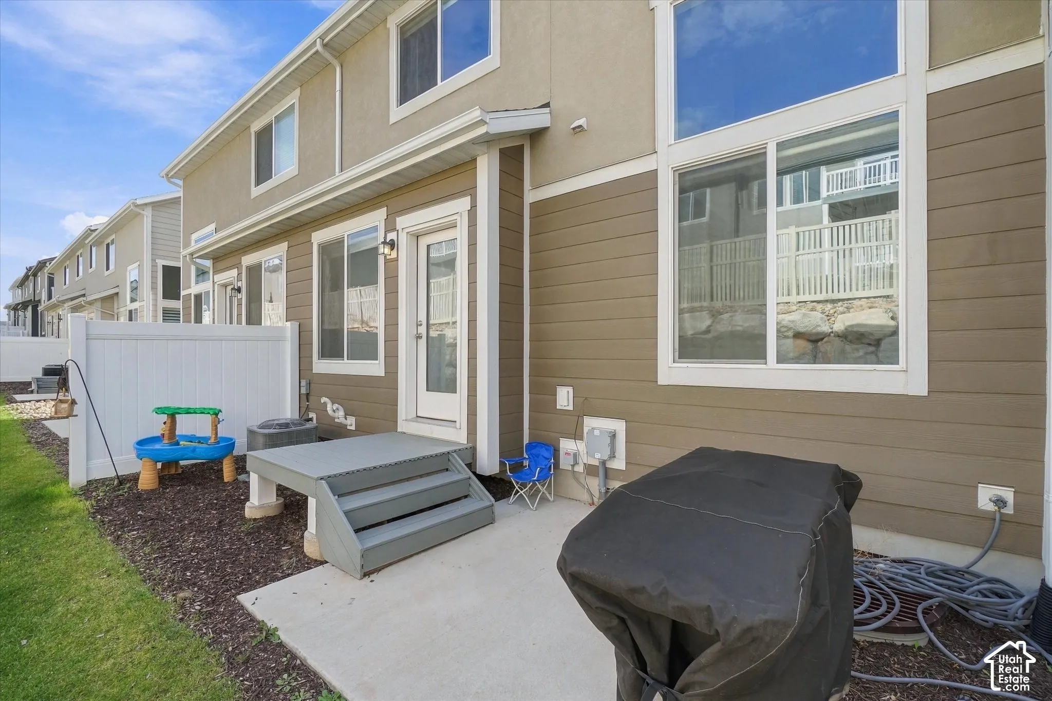 Exterior facade featuring horizontal siding and stucco, concrete patio, small raised landing with stairs, and white privacy fencing