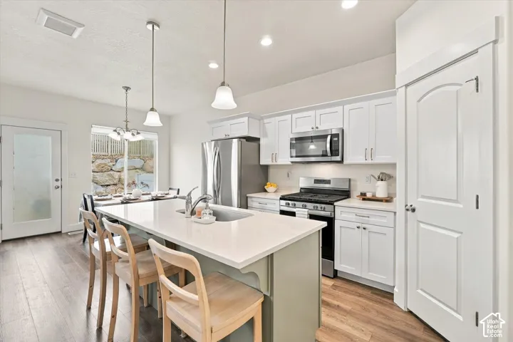 Kitchen featuring white cabinetry, quartz countertops, a central island with undermount sink, stainless steel appliances, and wood-finish flooring
