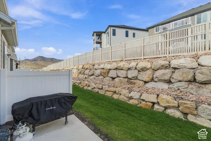 Outdoor space featuring a concrete patio, lawn area, tiered natural stone retaining wall, and vinyl privacy fencing