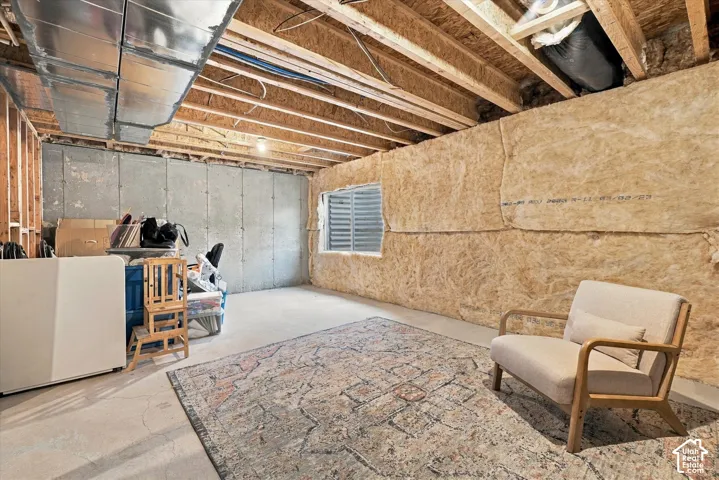 Unfinished space featuring exposed timber joist ceiling, concrete flooring, exterior-facing egress window with window well, and fiberglass wall insulation
