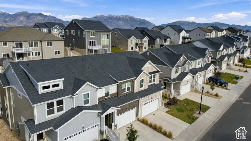 Aerial perspective of a multi-story residence featuring composite shingle roofing, vertical board-and-batten siding, stone veneer accents, multi-car garage, and a mountainous backdrop