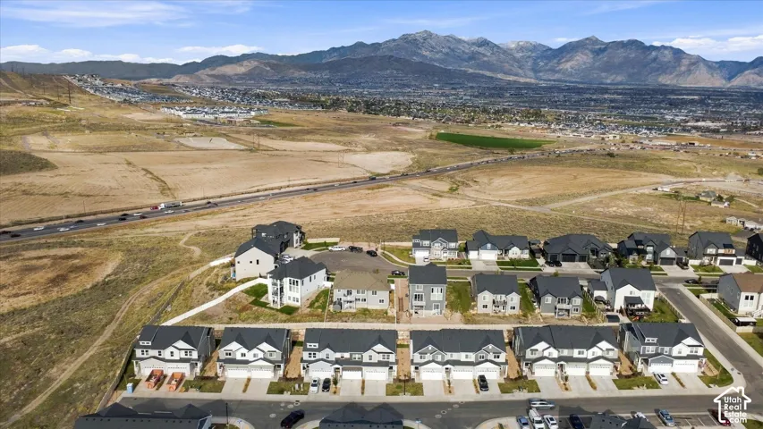 Aerial perspective of a multi-unit residential community featuring asphalt-shingled gable roofs, paved driveways, attached garages, and expansive mountain range backdrop