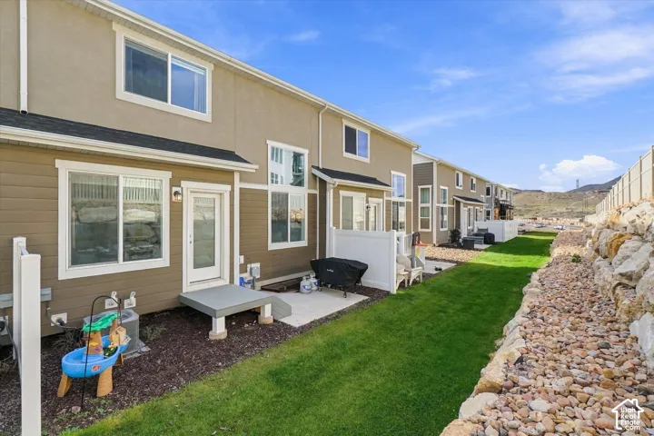 Exterior facade featuring horizontal siding, concrete rear patio, white vinyl privacy fencing, manicured lawn, and stone retaining wall
