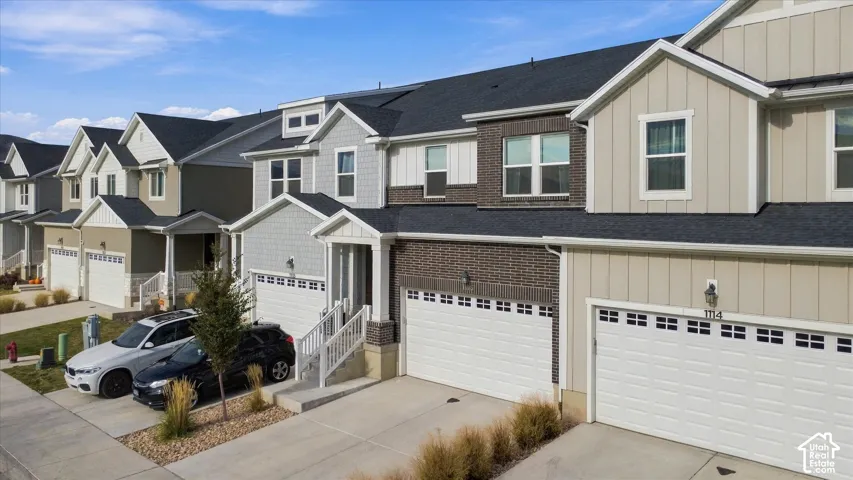 Multi-story townhome exterior featuring brick and vertical siding, pitched rooflines, dual-car garages, and white wooden porch railings