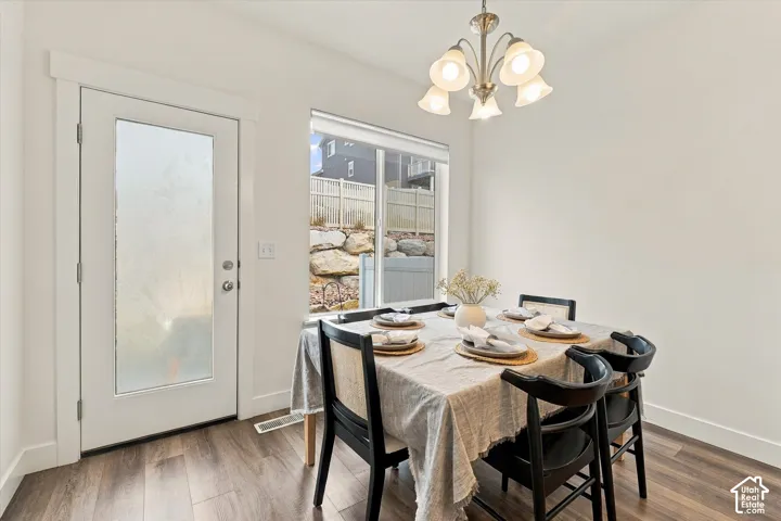 Neutral-toned interior featuring wood-finish flooring, a glass-panel exterior door, a large window with roller shade, and a multi-arm metallic light fixture