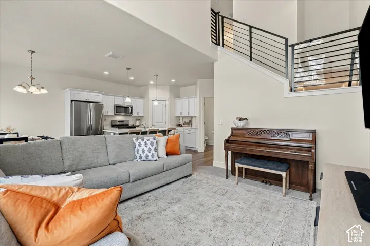 Open-concept floor plan featuring high ceilings, white cabinetry, stainless steel appliances, kitchen island, and metal horizontal-bar staircase railing